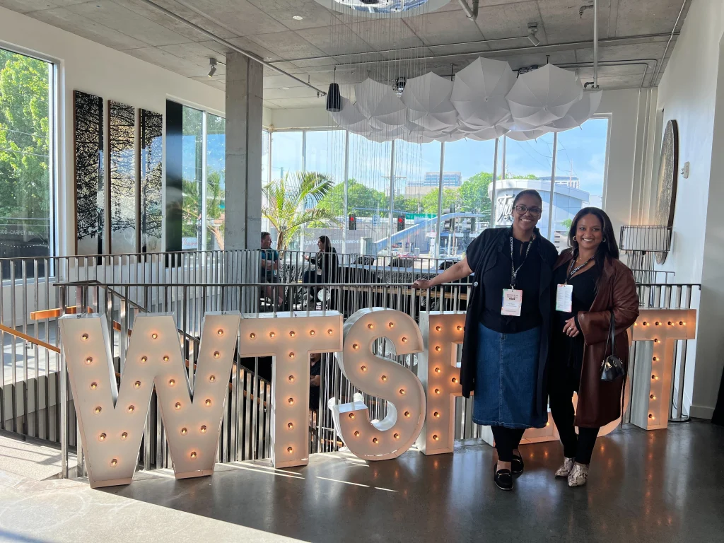 Malee Gunaratne and 
Iquo Inyang at WTSFest Portland, standing in front of large marquee letter signage at the conference venue